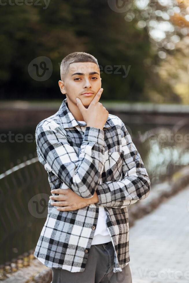 Vertical close-up portrait of a teenager in casual clothes. Happy smiling teenager in autumn park in sunlight. A beautiful child looks at the camera in nature. photo