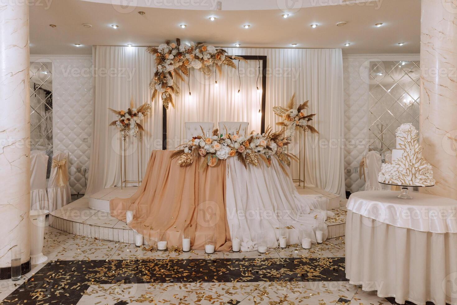 The wedding table of the bride and groom, decorated with flowers, dried ears of corn and white tulle, is made in nude color. Flowers on stands. Wedding details. light photo