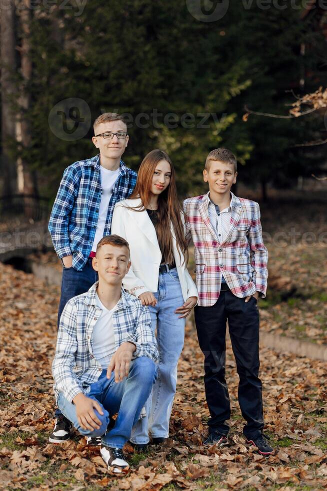 cuatro adolescentes de diferente sexos, posando en naturaleza. Adolescente compañeros de clase son descansando en contra el antecedentes de un otoño bosque. foto