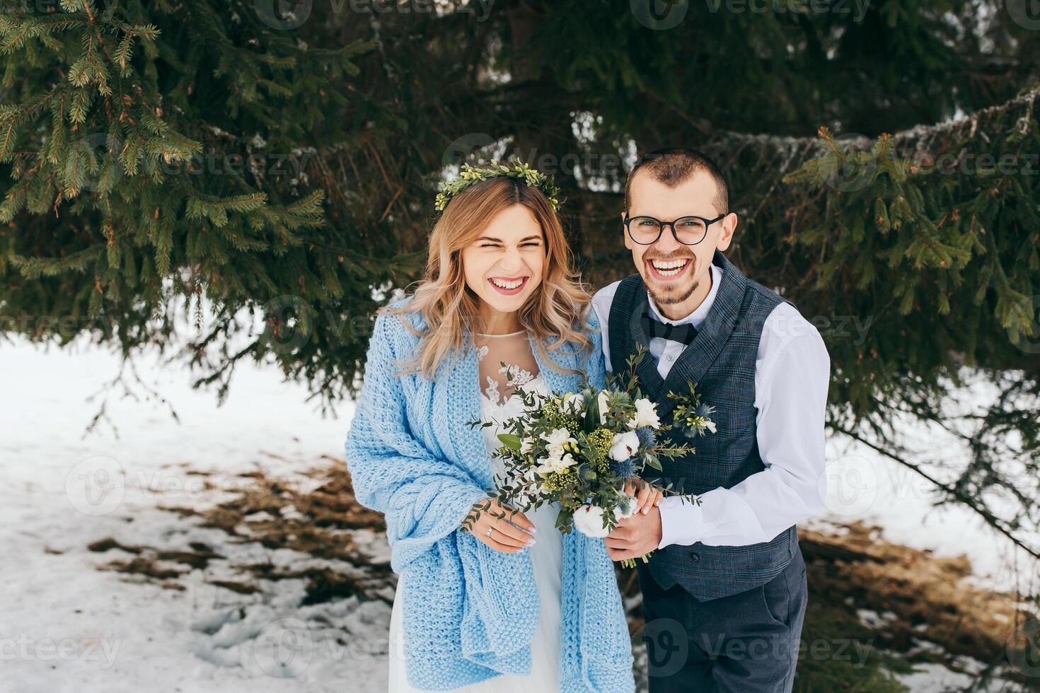 winter wedding in the mountains. Portrait of a happy and smiling bride and groom against the background of a winter forest. Beautiful bride and groom tenderly embrace. Modern winter wedding. photo