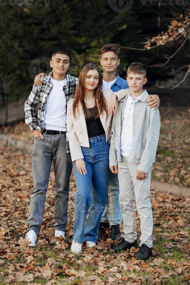 cuatro adolescentes de diferente sexos, posando en naturaleza. Adolescente compañeros de clase son descansando en contra el antecedentes de un otoño bosque. foto