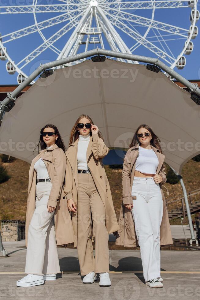 Three beautiful young teenage girls having fun together outdoors against the background of a ferris wheel in an Italian town. Urban lifestyle. City center. Best friends in casual clothes. photo