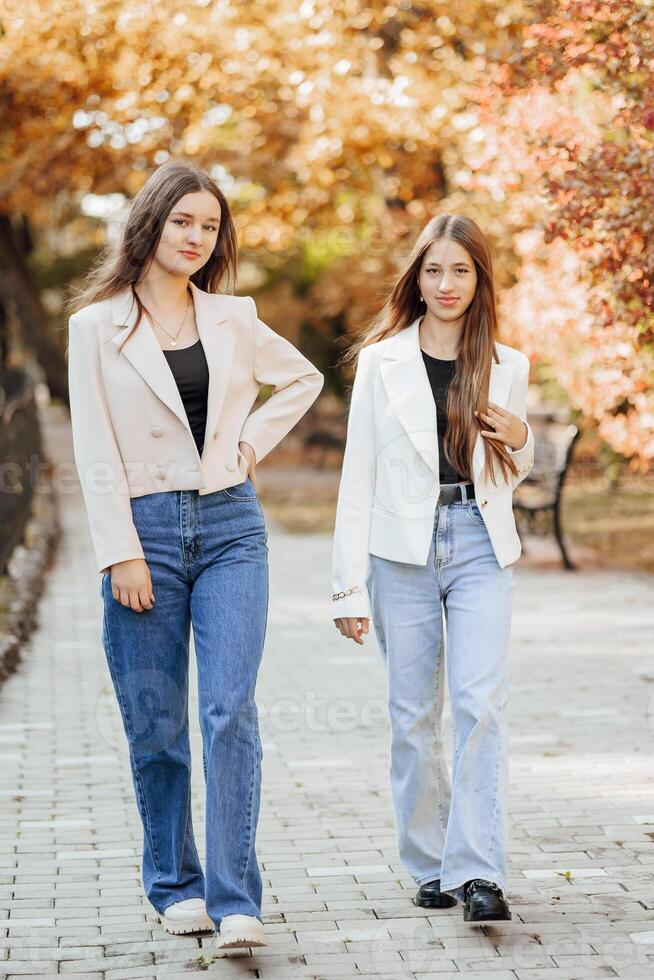 The two teenage sisters are dressed in casual clothes. Autumn in nature. They go to the front and look into the camera. Friendship of two sisters. Best Friends. Privacy from adults. photo