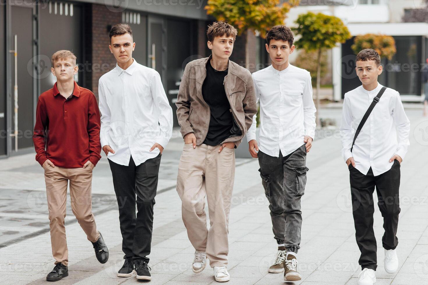 Group of smiling and happy teenage friends wearing casual clothes spending time together, posing and talking with each other near college building on autumn day. photo