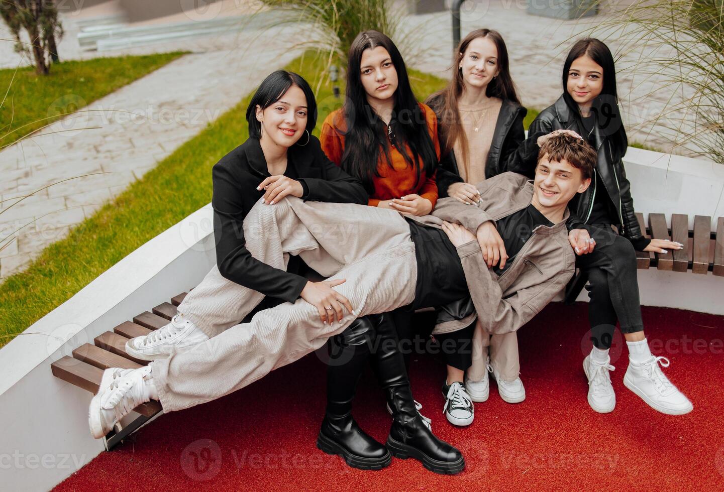 Group of smiling and happy teenage friends wearing casual clothes spending time together, posing and talking with each other near college building on autumn day. photo