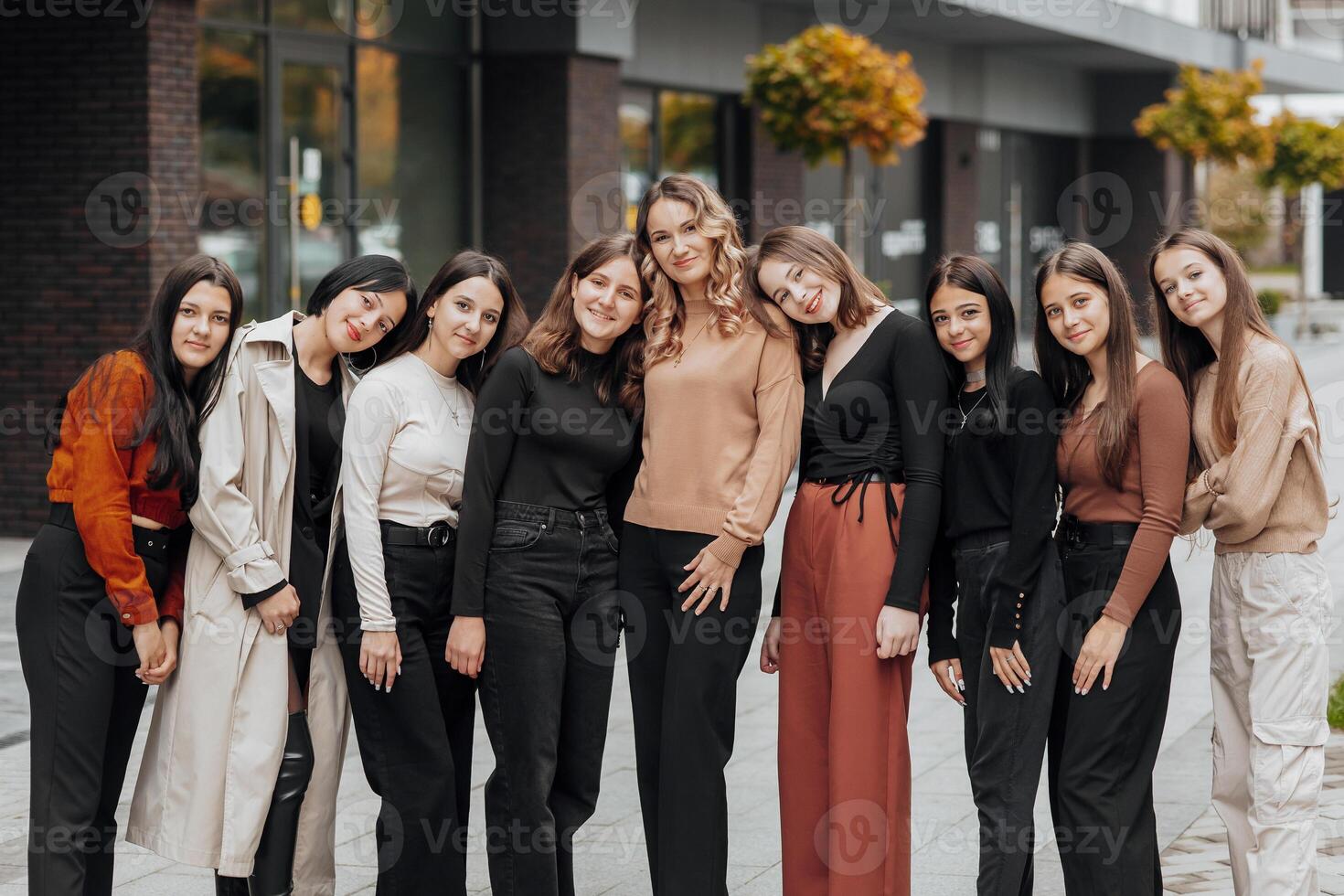 Group of smiling and happy teenage friends wearing casual clothes spending time together, posing and talking with each other near college building on autumn day. photo