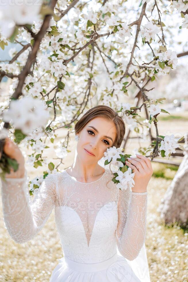 un Pelirrojo novia poses en contra el antecedentes de un floreciente árbol. magnífico vestir con largo mangas, abierto busto. primavera Boda foto