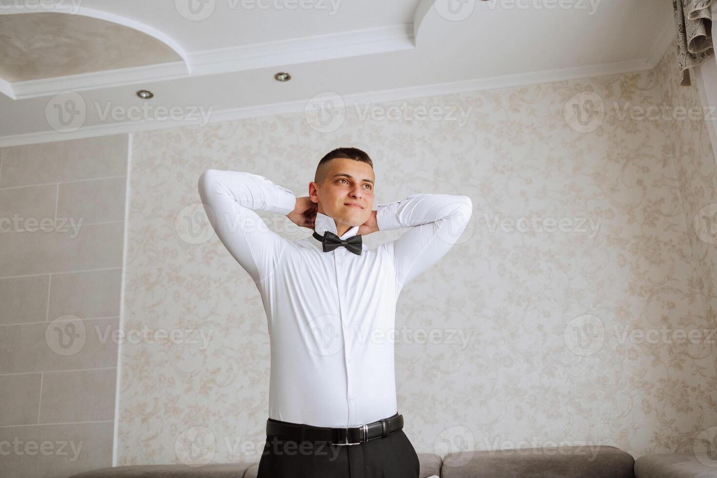 A stylish groom is tying his tie, preparing for the wedding ceremony. Groom's morning. A businessman wears a tie. The groom is getting ready in the morning before the wedding ceremony. photo