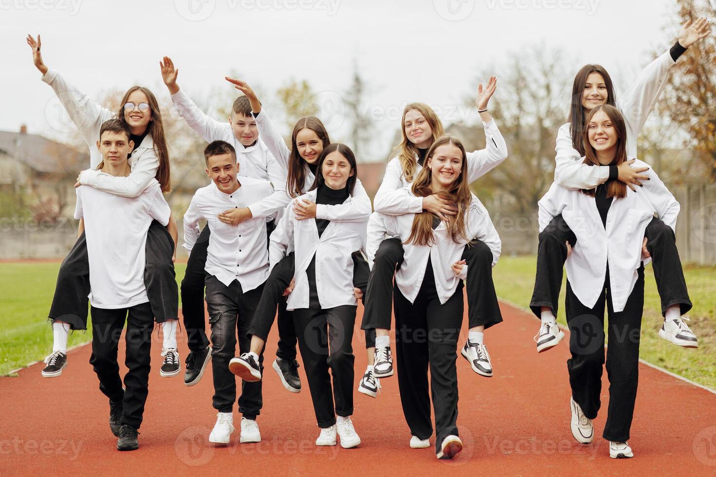 A group of many happy teenagers dressed in the same outfit having fun and posing in a stadium near a college. Concept of friendship, moments of happiness. School friendship photo