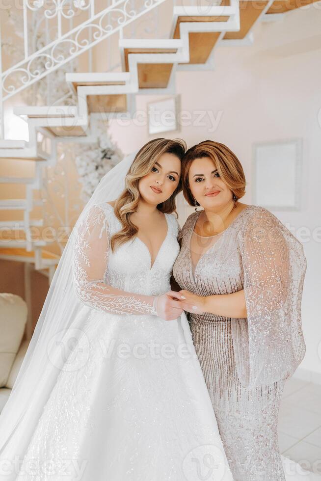 A beautiful and happy mother and her daughter, the bride, are standing next to each other. The best day for parents. Tender moments at the wedding. photo