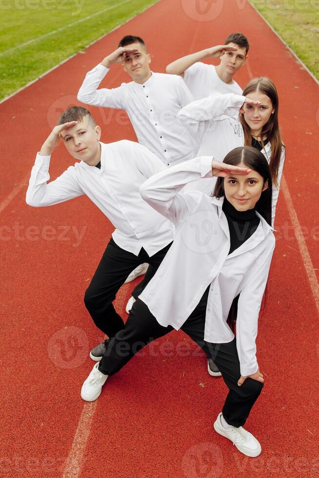 un grupo de sonriente y contento Adolescente amigos, vestido en casual ropa, gastar hora juntos, actitud y tener divertido en el jardines de un educativo institución en un otoño día. foto