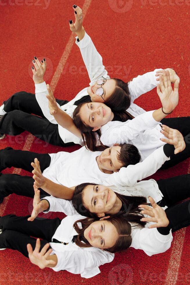 Happy friends lying together in a circle looking at the camera, holding hands and smiling while lying on a red wall... Friendship, lifestyle, togetherness, business and teamwork concepts. photo