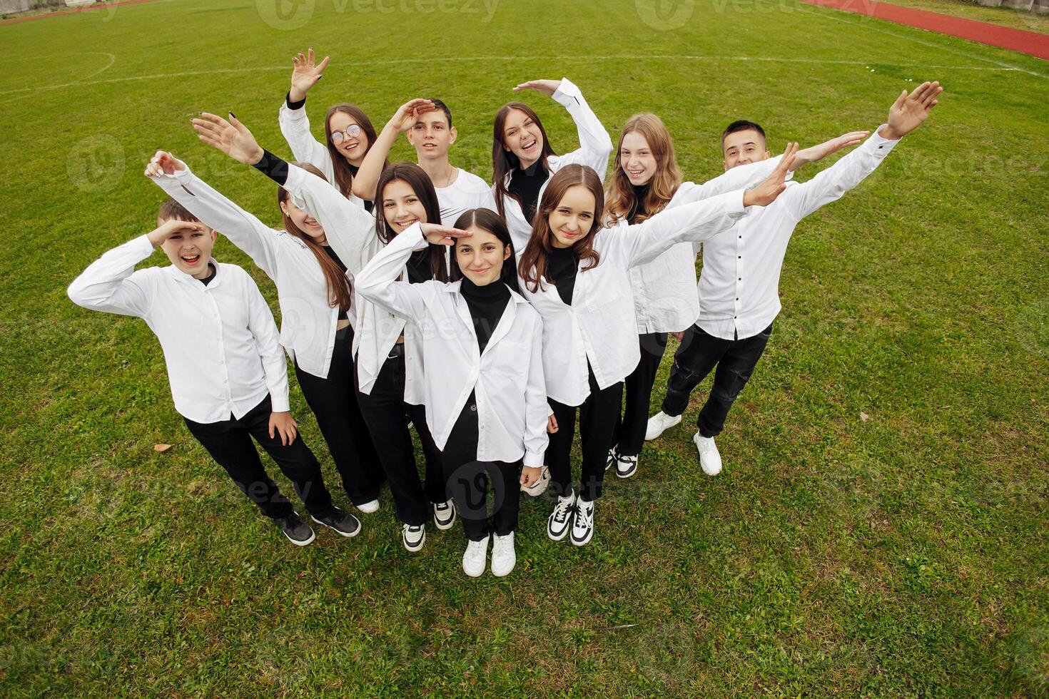 un grupo de muchos contento adolescentes vestido en el mismo atuendo teniendo divertido y posando en un estadio cerca un colega. concepto de amistad, momentos de felicidad. colegio amistad foto