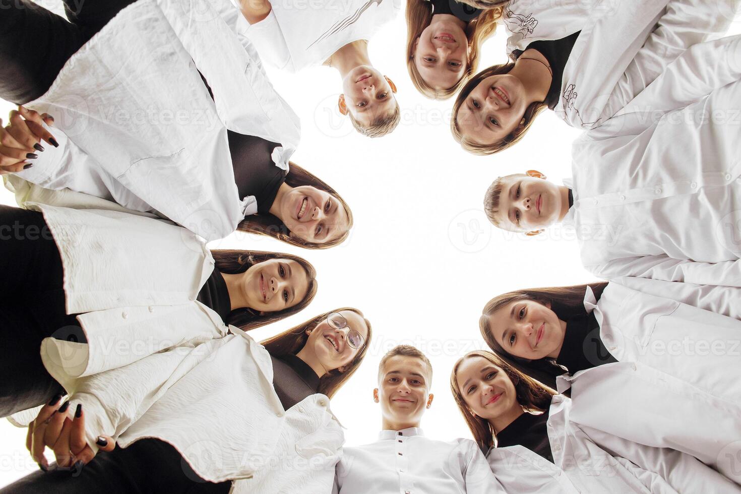 grande grupo de sonriente joven personas de pie, abrazando, mirando a cámara. grupo de alegre Adolescente personas en un circulo mirando abajo. bajo visita ángulo. Copiar espacio. foto