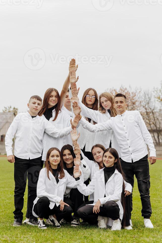 A group of many happy teenagers dressed in the same outfit having fun and posing in a stadium near a college. Concept of friendship, moments of happiness. School friendship photo