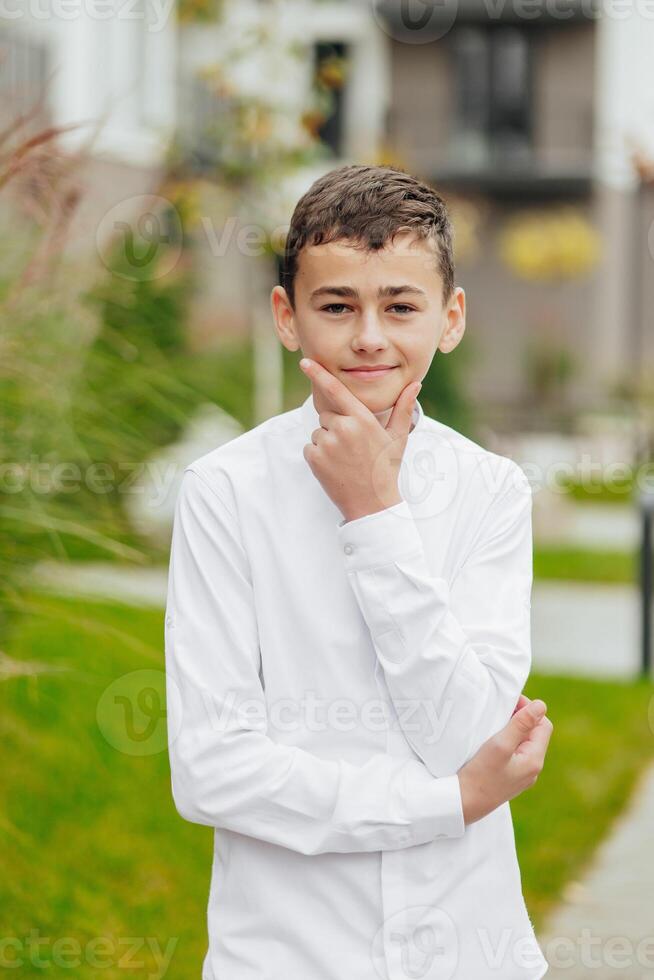 Vertical close-up portrait of a teenager in casual clothes. Happy smiling teenager in autumn park in sunlight. A beautiful child looks at the camera in nature. photo