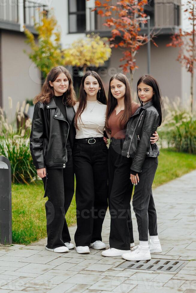 Group of smiling and happy teenage friends wearing casual clothes spending time together, posing and talking with each other near college building on autumn day. photo