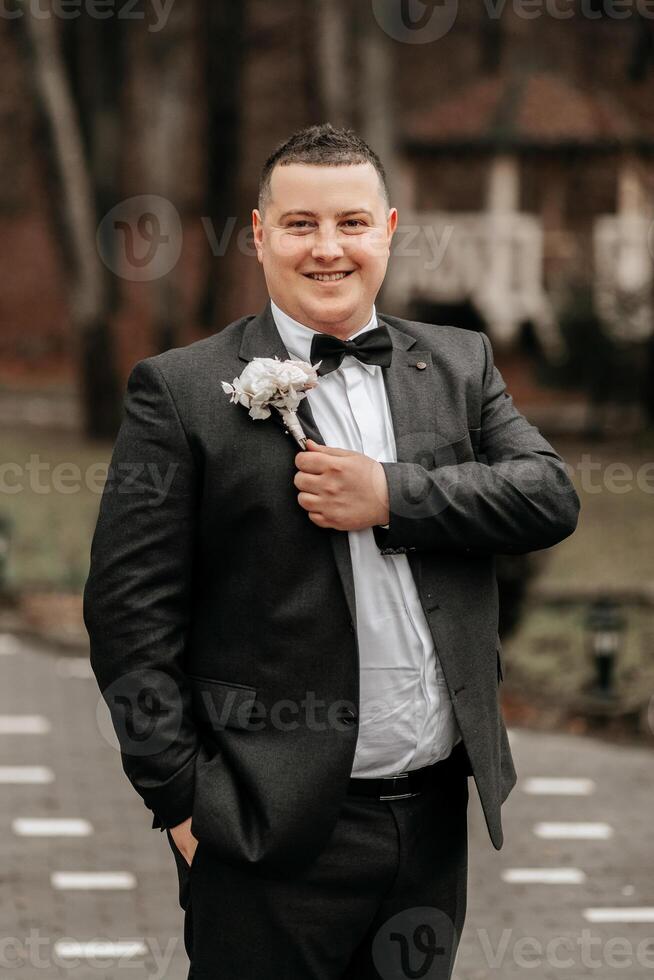 portrait of a handsome and manly groom in a black suit with a tie. Groom in nature in the winter season. photo