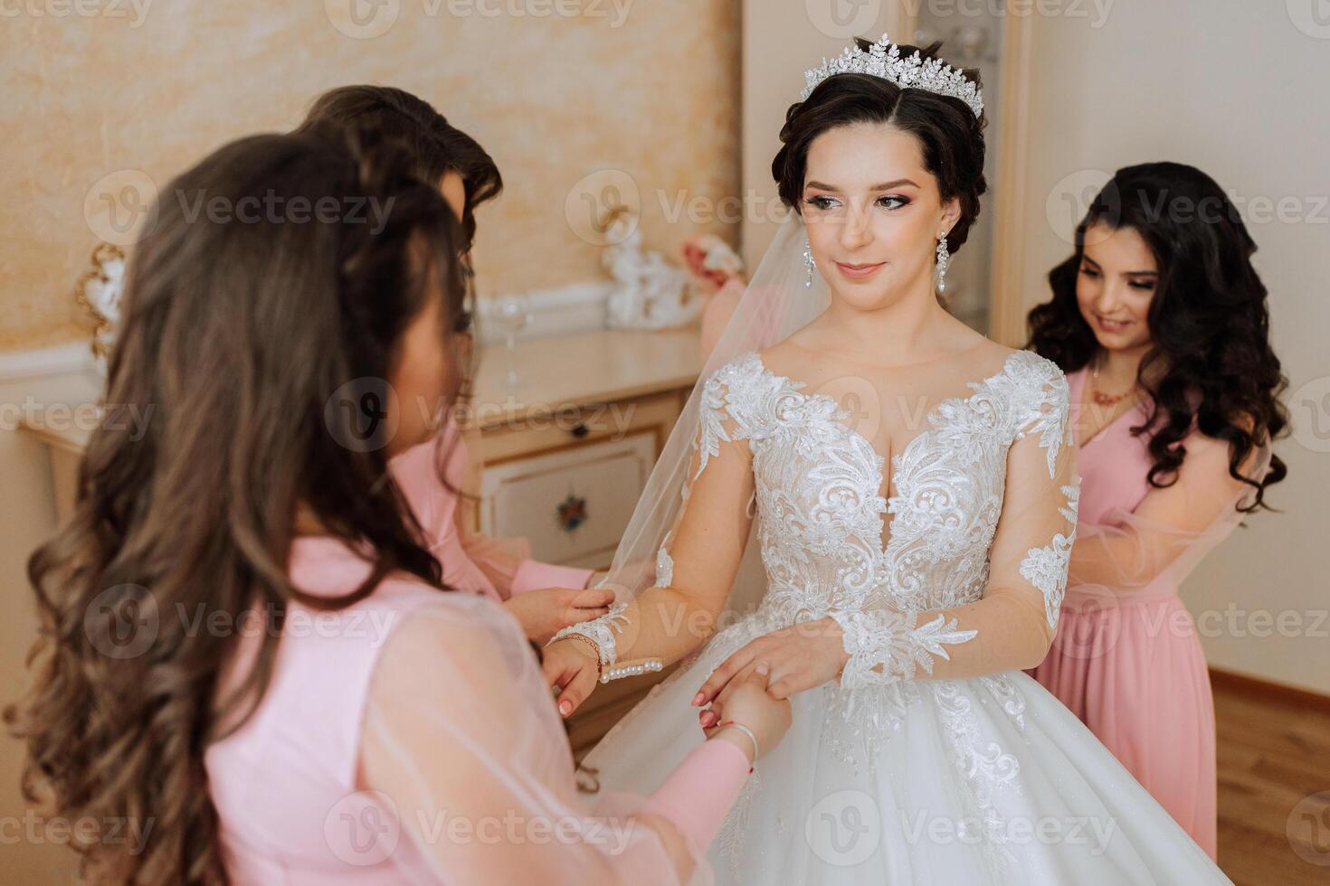 A friend helps the bride fasten her dress. A woman helps her friend fasten the buttons on the back of her wedding dress. The morning of the bride, the creation of a family, an important event. photo