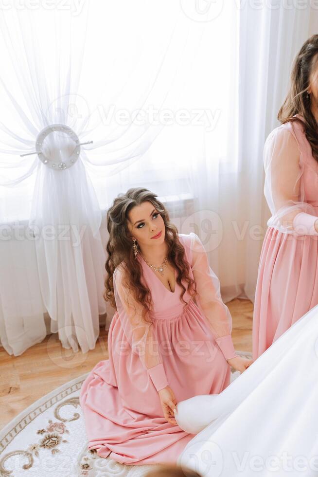 un amigo ayuda el novia sujetar su vestido. un mujer ayuda su amigo sujetar el botones en el espalda de su Boda vestido. el Mañana de el novia, el creación de un familia, un importante evento. foto