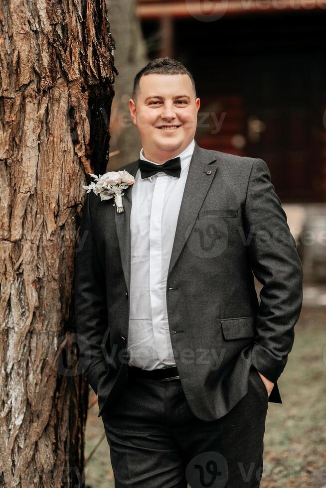 portrait of a handsome and manly groom in a black suit with a tie. Groom in nature in the winter season. photo