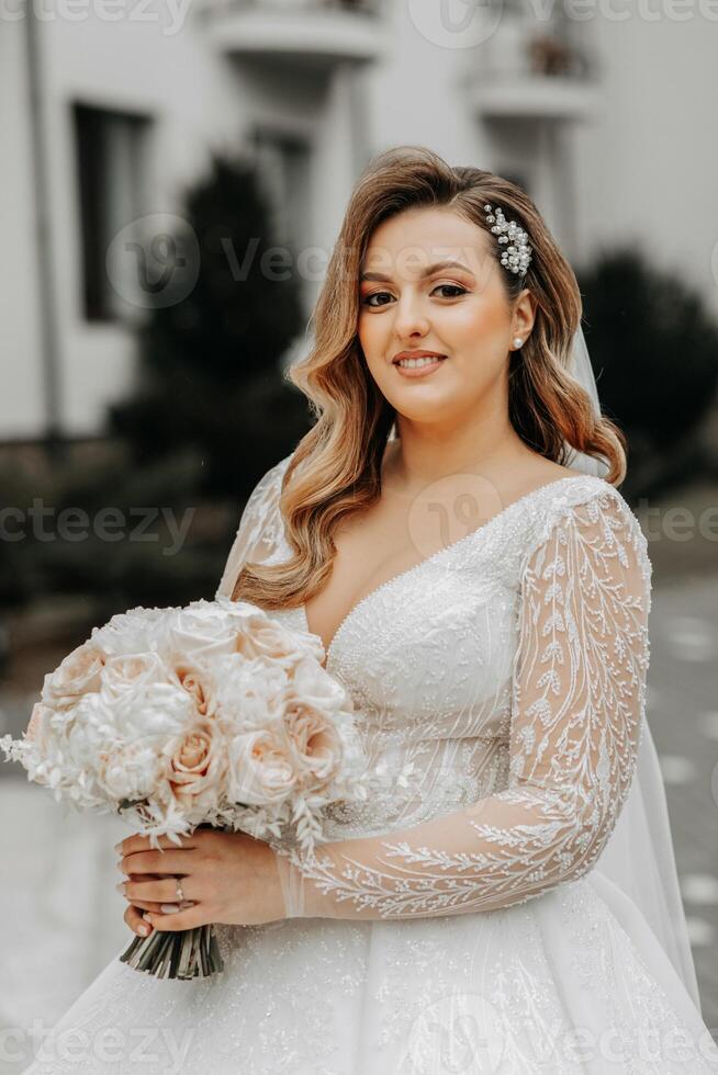 Portrait of a beautiful bride with a wedding bouquet of flowers, attractive woman in a wedding dress with a long veil. Happy bride woman. Bride with wedding makeup and hairdo. Winter wedding photo