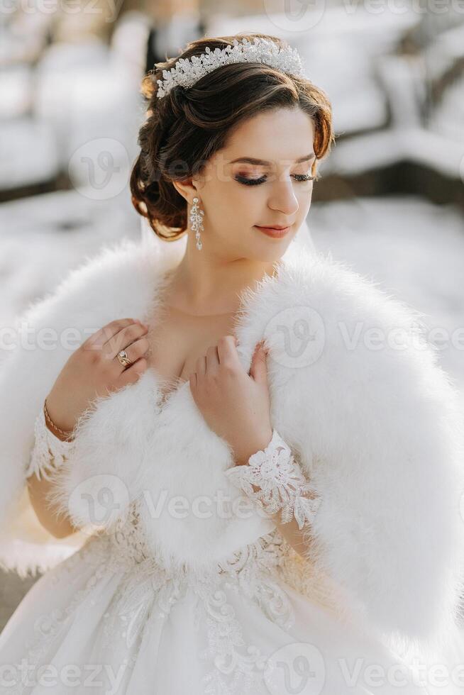 Portrait of a beautiful bride with a wedding bouquet of flowers, attractive woman in a wedding dress with a long veil. Happy bride woman. Bride with wedding makeup and hairdo. Winter wedding photo