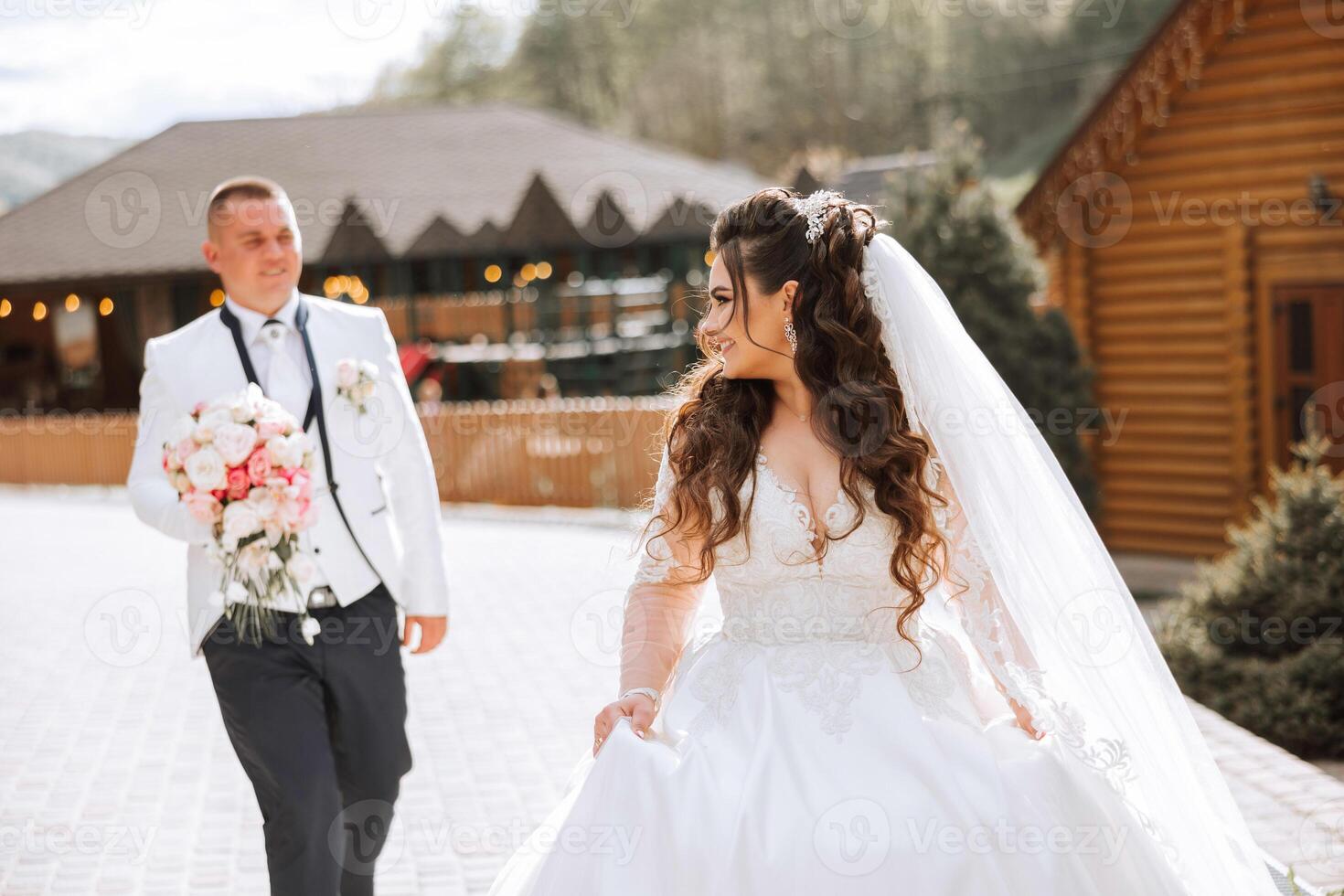 A beautiful young bride, in a summer park, walks ahead of her groom. Beautiful wedding white dress. Walks in the park. A happy and loving couple. photo