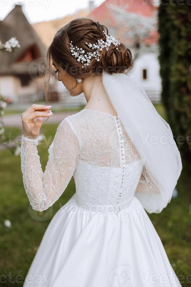 un Pelirrojo novia en un elegante vestir con largo mangas y un hermosa ornamento en su cabello, posando con su espalda convertido a el cámara. primavera Boda foto