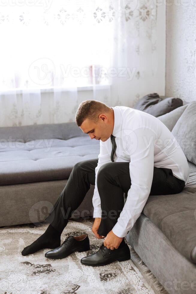 A man's hands tie the laces of his new shoes. People, business, fashion and footwear concept - close-up of a man's legs and hands tying shoelaces. The groom puts on his shoes. photo