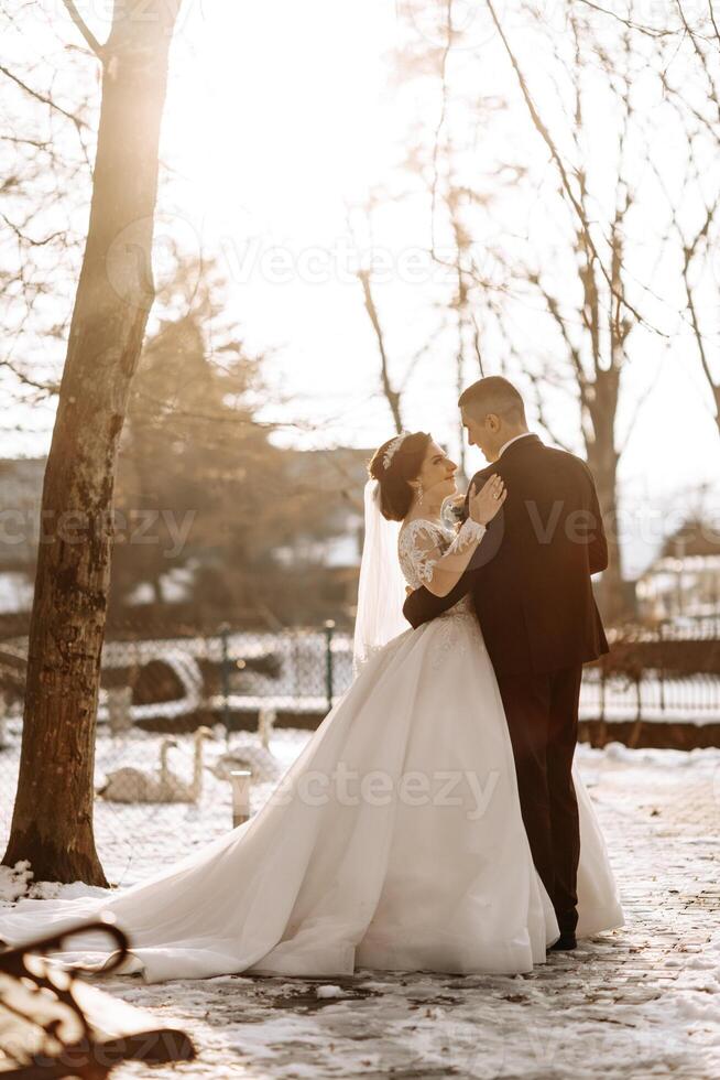 Winter wedding. A happy couple in wedding clothes are hugging and smiling in a winter park covered with snow on their wedding day. Winter love story of a beautiful couple in snowy winter weather photo