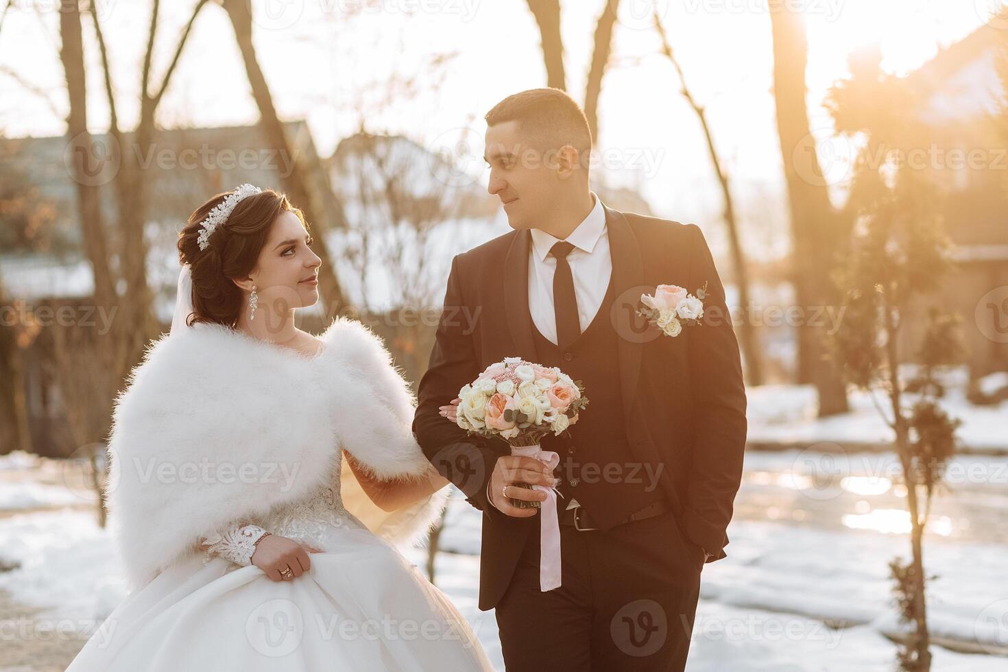 Winter wedding. Happy couple walking in wedding clothes hugging and smiling in a winter park covered with snow on their wedding day. Winter love story of a beautiful couple in snowy winter weather photo