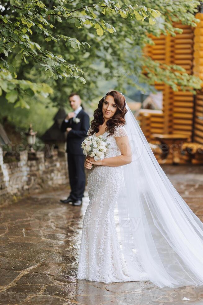 A beautiful young bride, in a summer park, walks ahead of her groom. Beautiful wedding white dress. Walks in the park. A happy and loving couple. photo