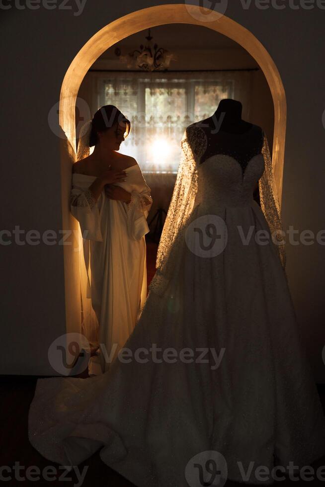 A beautiful brunette bride with a tiara in her hair is getting ready for the wedding in a beautiful robe in boudoir style. Close-up wedding portrait, photo. photo