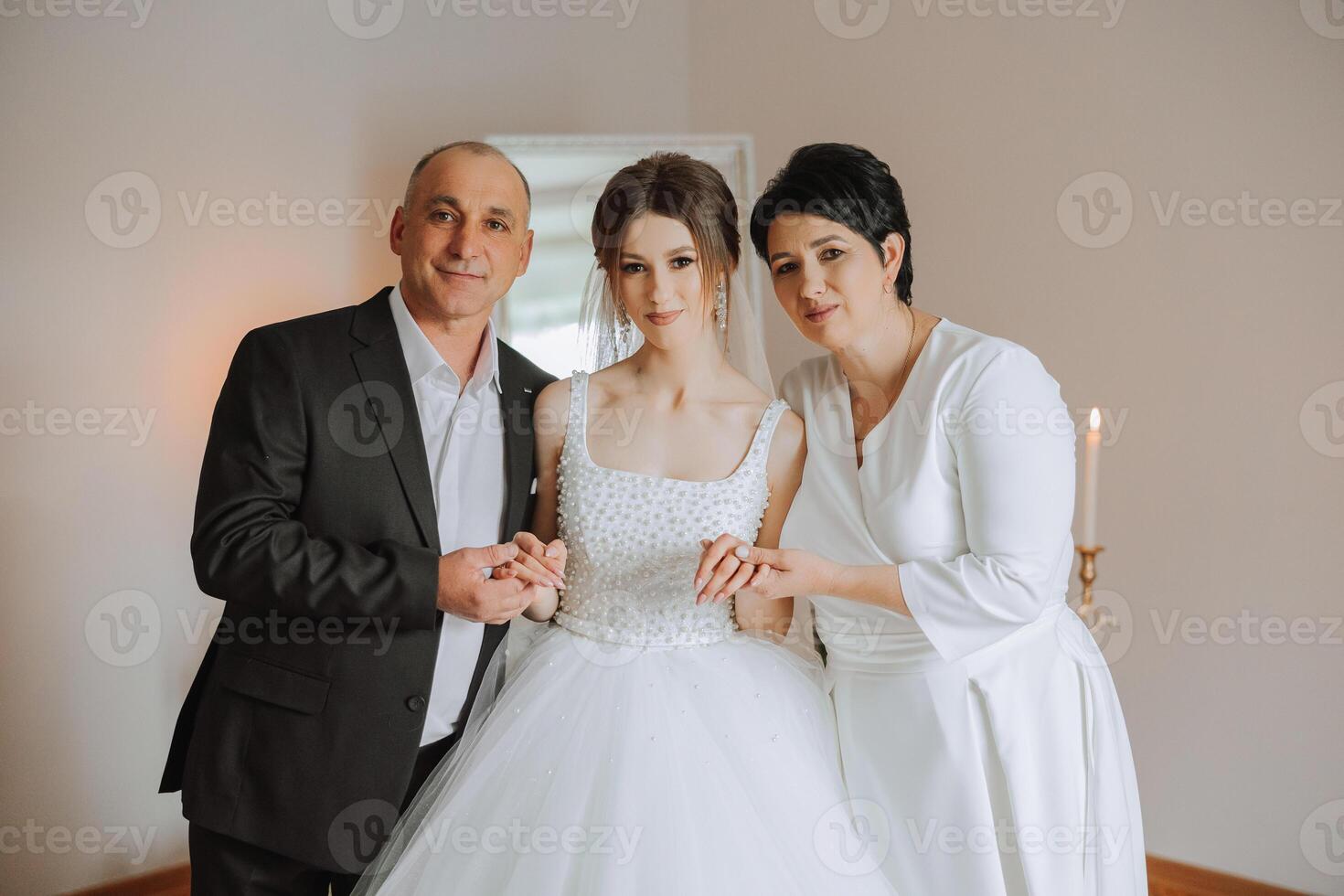 Happy parents hold the hands of the bride who is getting married and support her, wearing a wedding dress and a long veil. photo