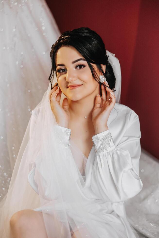 A beautiful brunette bride with a tiara in her hair is getting ready for the wedding in a beautiful robe in boudoir style. Close-up wedding portrait, photo. photo