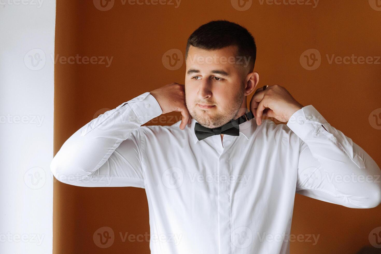 A stylish groom is tying his tie, preparing for the wedding ceremony. Groom's morning. A businessman wears a tie. The groom is getting ready in the morning before the wedding ceremony. photo