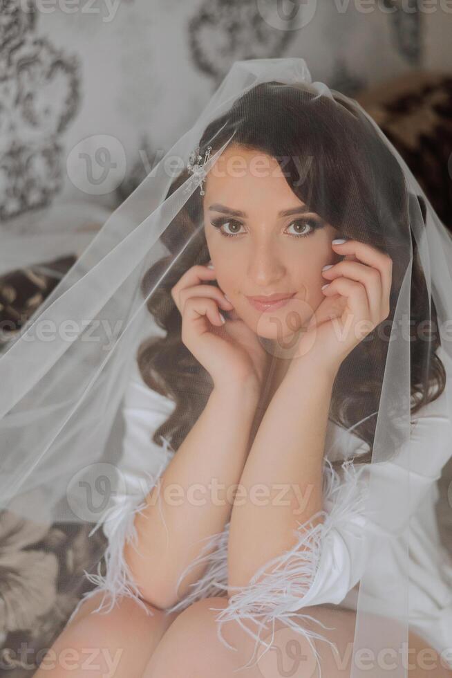 un hermosa morena novia con un tiara en su pelo es consiguiendo Listo para el Boda en un hermosa túnica en tocador estilo. de cerca Boda retrato, foto. foto