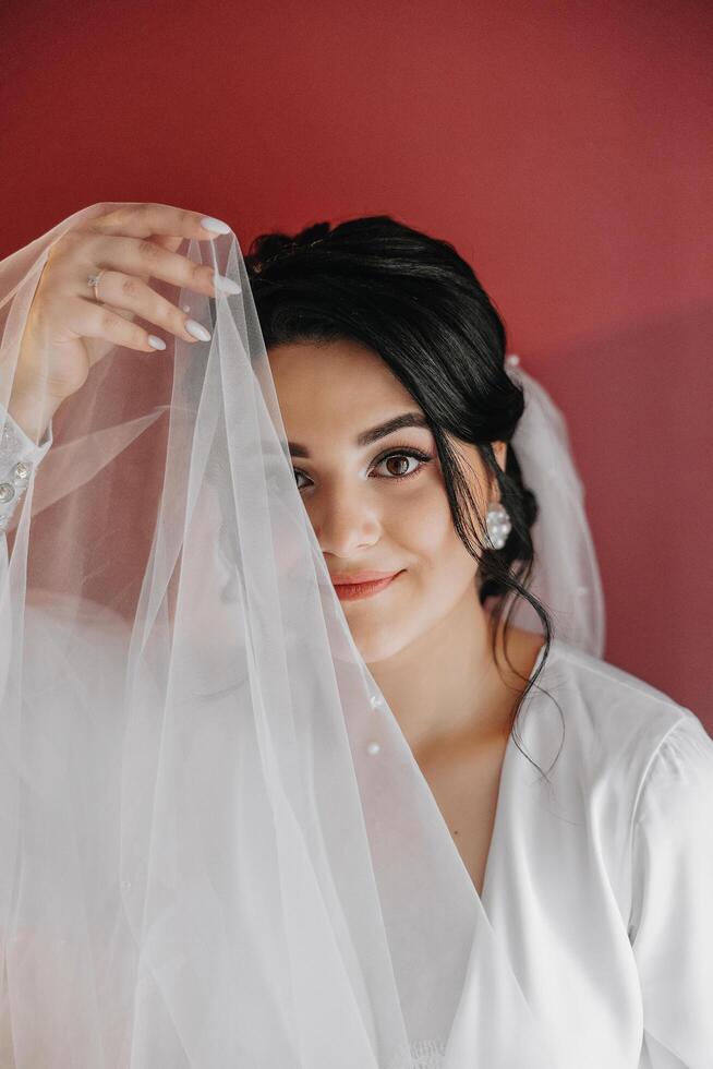 A beautiful brunette bride with a tiara in her hair is getting ready for the wedding in a beautiful robe in boudoir style. Close-up wedding portrait, photo. photo