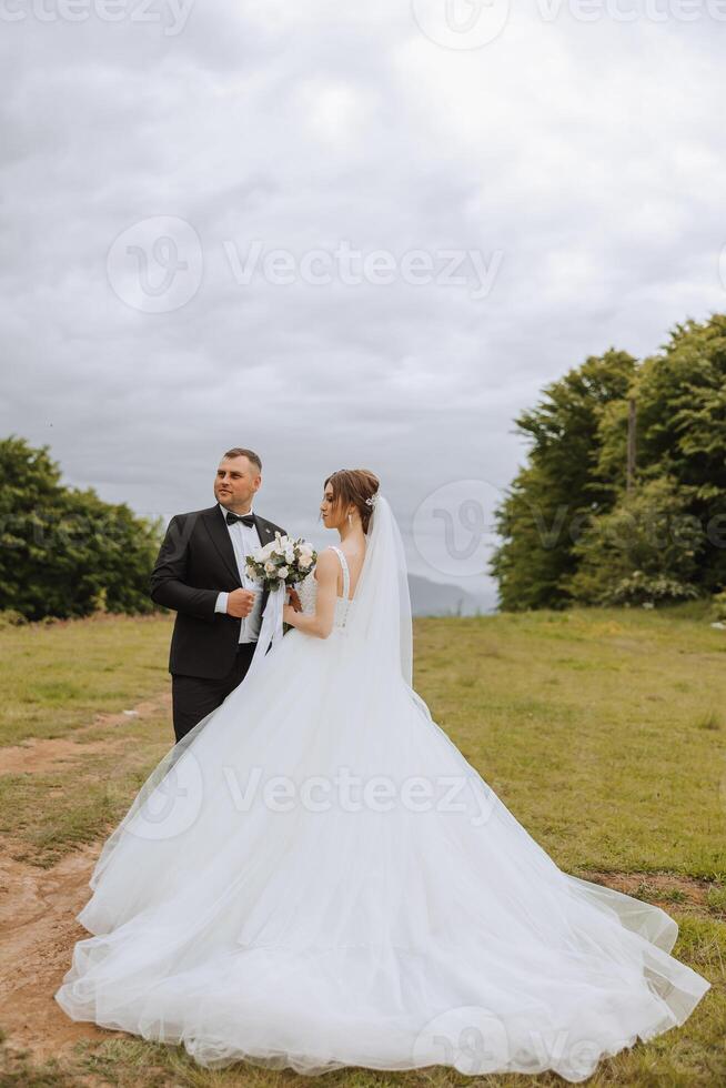 A beautiful young bride, in a summer park, walks ahead of her groom. Beautiful wedding white dress. Walks in the park. A happy and loving couple. photo