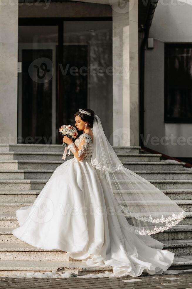 hermosa novia con un Boda ramo de flores de flores, atractivo mujer en un Boda vestir con un largo velo. contento novia mujer. novia con Boda maquillaje y peinado. invierno Boda foto