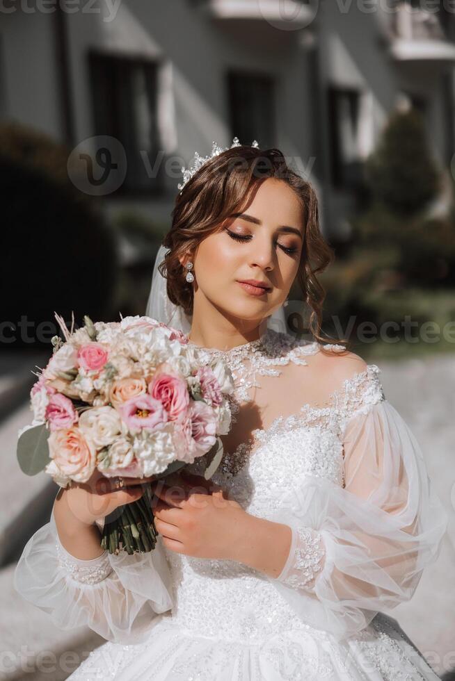 morena novia en fuera del hombro cordón blanco vestir y tiara posando con un ramo de flores de blanco y rosado flores hermosa pelo y constituir. primavera Boda foto