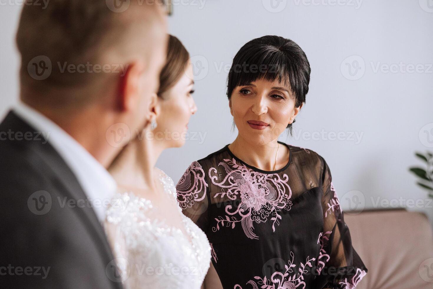 Happy parents hold the hands of the bride who is getting married and support her, wearing a wedding dress and a long veil. photo