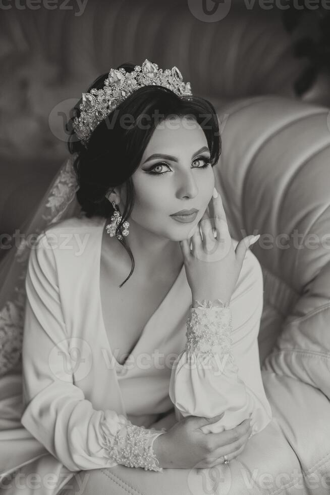 A beautiful brunette bride with a tiara in her hair is getting ready for the wedding in a beautiful robe in boudoir style. Close-up wedding portrait, photo. photo