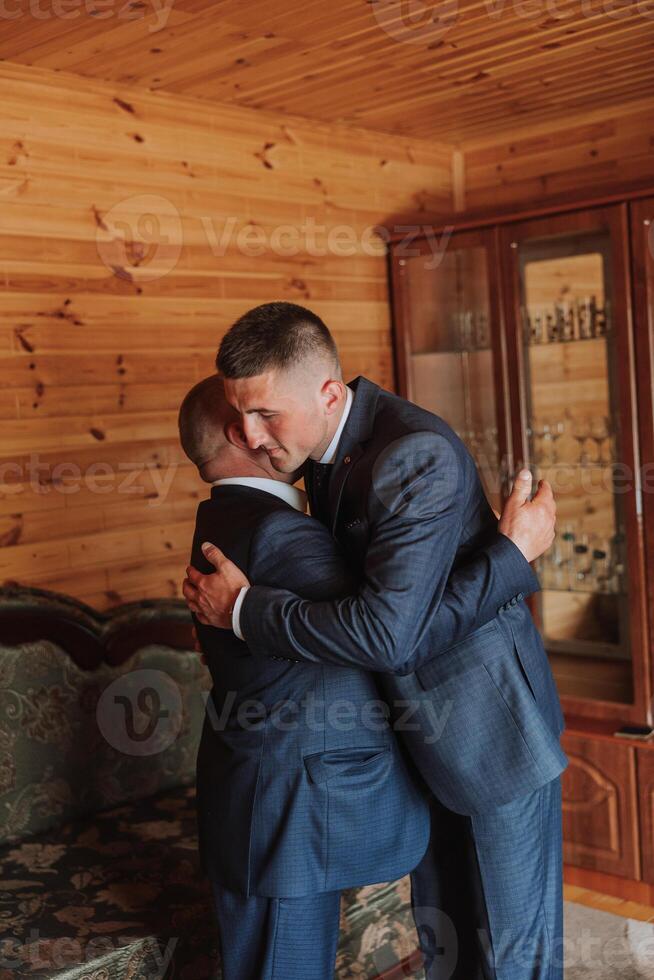 A father hugs his mature son and helps him prepare for the wedding ceremony. Warm and sincere relations between a father and an adult son. An emotional moment at a wedding photo