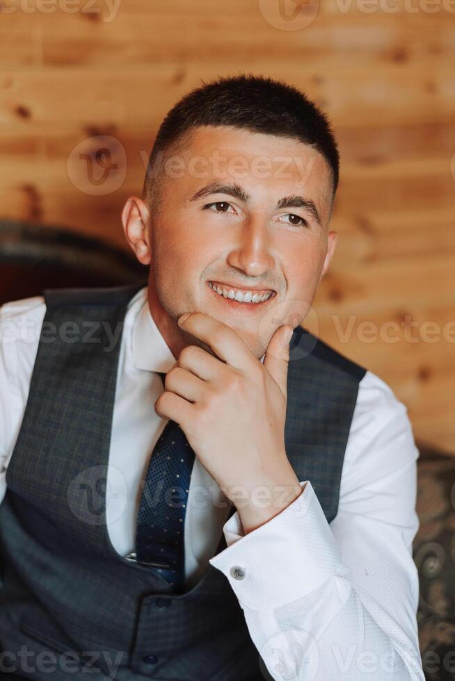 A stylish portrait of the groom preparing for the wedding ceremony in the morning. Groom's morning. Preparation for the groom's morning. The groom puts on a jacket. The confident look of a mature man. photo