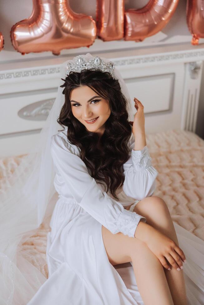 A beautiful brunette bride with a tiara in her hair is getting ready for the wedding in a beautiful robe in boudoir style. Close-up wedding portrait, photo. photo