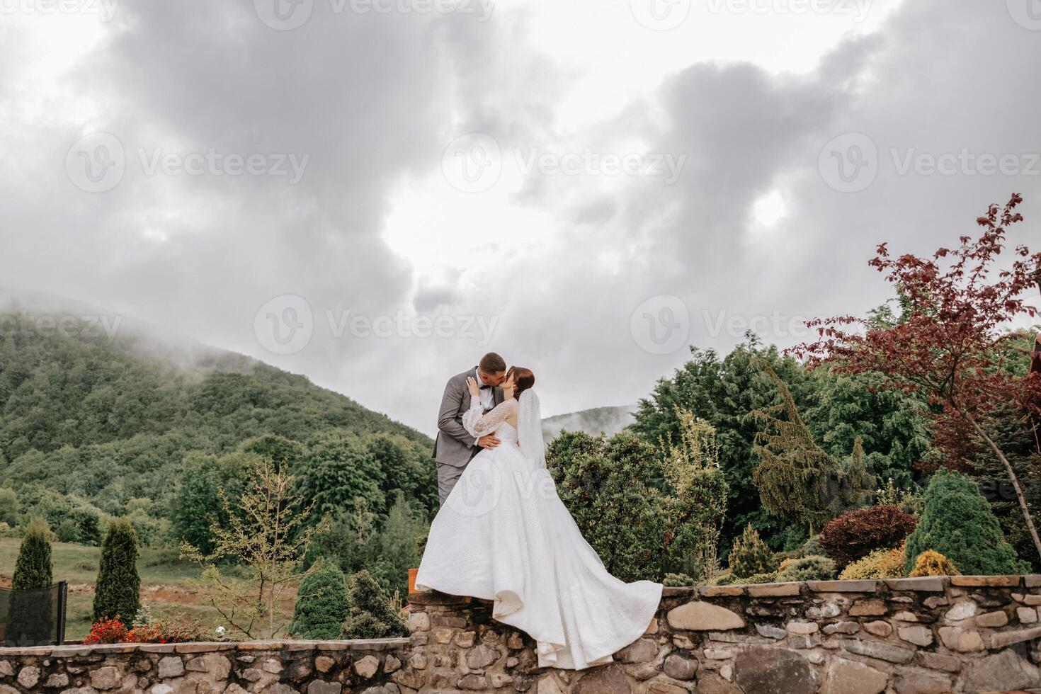 boda. amor y Pareja en jardín para boda. celebracion de ceremonia y compromiso. salvar el fecha. confianza. el novio abraza el novia en contra el antecedentes de montañas y un nublado cielo. foto