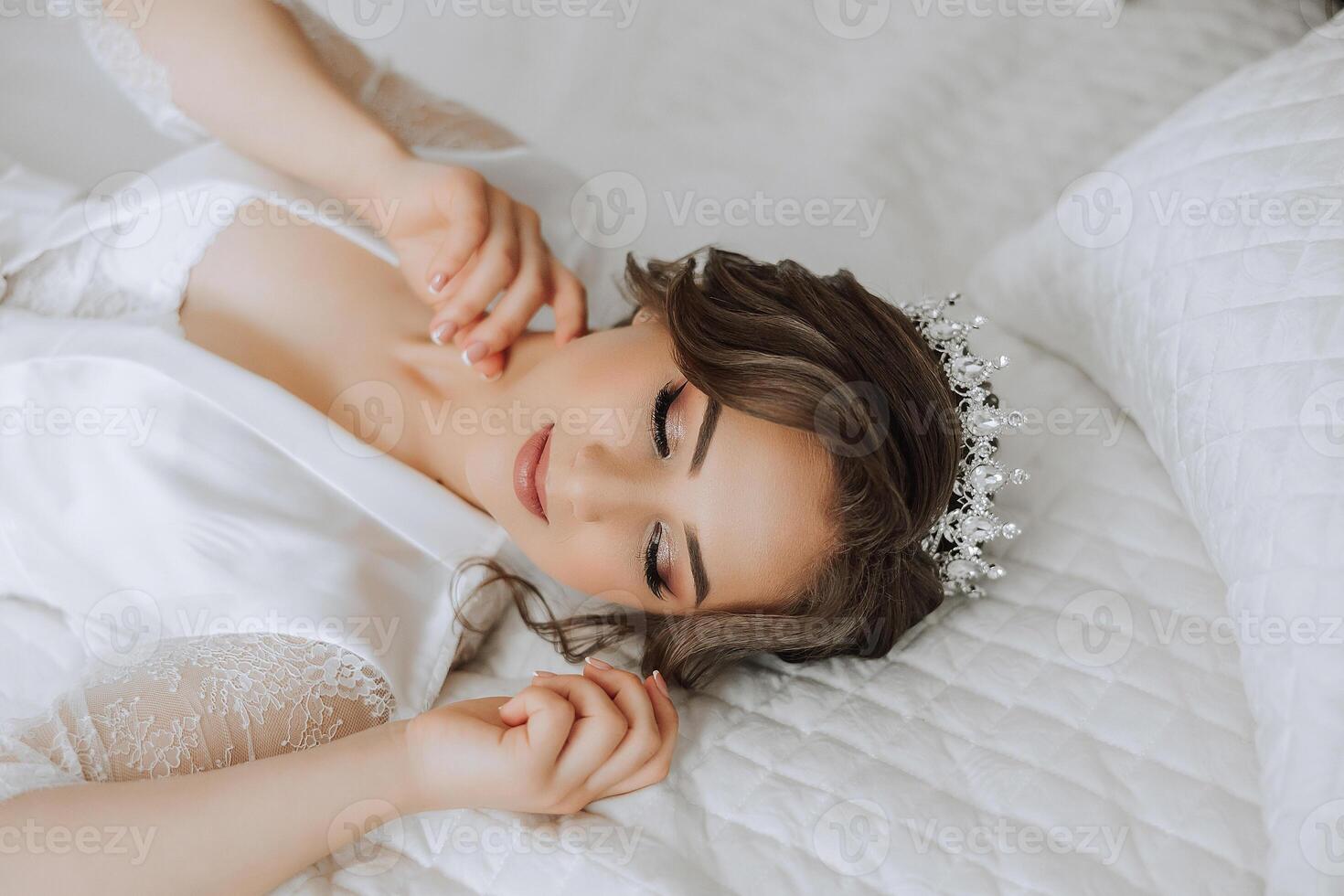 A beautiful brunette bride with a tiara in her hair is getting ready for the wedding in a beautiful robe in boudoir style. Close-up wedding portrait, photo. photo