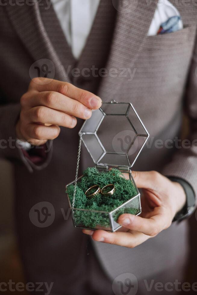 Golden wedding rings in a glass gift box, in the hands of the groom, close-up. Wedding concept. Wedding details. photo